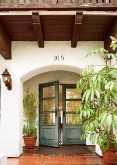 the front entrance to an elegant home with potted plants on either side and two large green doors