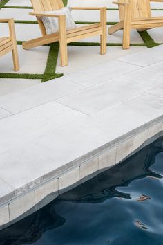 two wooden chairs sitting on top of a cement slab next to a small pool with water