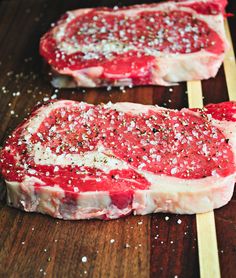 two pieces of raw meat sitting on top of a wooden cutting board with seasoning