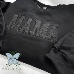 Elevate your mom style with our Mama Black Embroidered Glitter Vinyl Crewneck Sweatshirt! Made with high-quality materials, this cozy black sweatshirt is embroidered with the word "Mama" in a bold and chic font. The shimmering black glitter vinyl adds a touch of glamour, while the crewneck design provides comfort and style. Perfect for any mama looking to show off her love and style at the same time! THIS IS A PHYSICAL PRODUCT. CREWNECK IS UNISEX. CREWNECK IS EMBROIDERED. CREWNECK CONTAIN GLITTE Black Casual Sweatshirt With Embroidered Text, Casual Black Sweatshirt With Embroidered Text, Black Top With Custom Embroidery For Winter, Black Tops With Custom Embroidery For Winter, Black Sweatshirt With Custom Embroidery For Fall, Casual Long Sleeve Sweatshirt With Glitter Print, Casual Long Sleeve Glitter Print Sweatshirt, Casual Glitter Print Long Sleeve Sweatshirt, Black Embroidered Text Sweatshirt Crew Neck