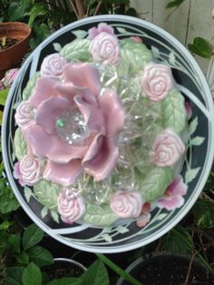 a pink flower sitting on top of a glass plate next to some potted plants