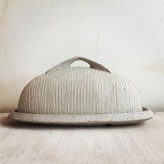 a white ceramic covered dish sitting on top of a wooden table next to a wall