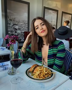 a woman sitting at a table with a plate of french fries and a glass of wine