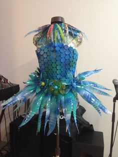 a mannequin made out of blue and green plastic bottles with feathers on it