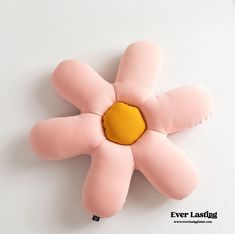 a pink and yellow flower shaped pillow sitting on top of a white table next to a black cord