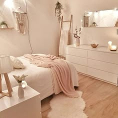 a bedroom with white furniture and lights on the wall, along with a bed covered in a pink blanket