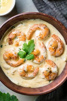 a bowl filled with shrimp and cream sauce on top of a white table next to some parsley