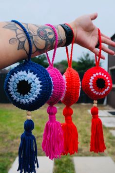 the hand is holding three crocheted balls with tassels hanging from them