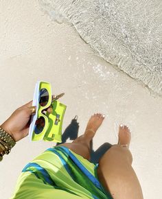 a woman is sitting on the beach with her feet in the sand and wearing sunglasses