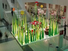 people are walking through an indoor mall with tall green plants and flowers on display in front of them