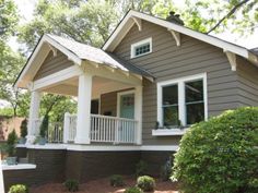 a gray house with white trim on the front porch and two story windows, surrounded by trees