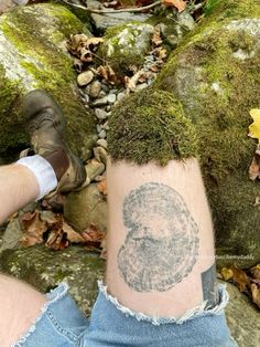 a person with a tattoo on their leg next to some rocks and leaves in the woods