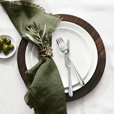 an empty plate with silverware and olives on it next to a green napkin