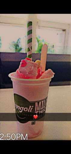 an ice cream sundae with toppings in a plastic cup on a table next to a window