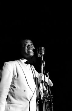 a black and white photo of a man in a tuxedo singing into a microphone