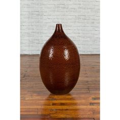 a large brown vase sitting on top of a wooden floor next to a brick wall