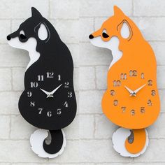 two clocks that look like animals are on the side of a brick wall, one is orange and the other is black