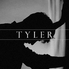 a man standing in front of a curtain with the word tyler over his head and hands behind him