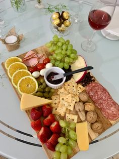 a platter of cheese, fruit and crackers on a table with wine glasses