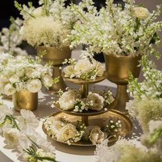 a table topped with three tiered trays filled with white flowers and greenery