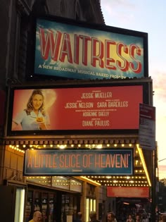 the marquee for waitress is lit up at dusk with people walking around it