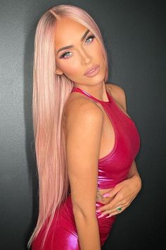 a woman with long pink hair wearing a red dress and looking at the camera while standing in front of a black wall