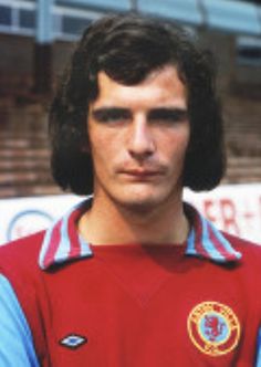 a young man wearing a red and blue shirt standing in front of a soccer field