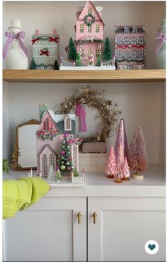 a shelf filled with christmas decorations on top of a white counter next to a pink house