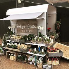 an outdoor flower shop with lots of plants and flowers on the shelves in front of it