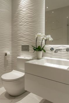 a white toilet sitting in a bathroom next to a sink and a vase with flowers