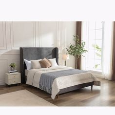 a bedroom with white walls and wood floors, a bed that has a gray upholstered headboard