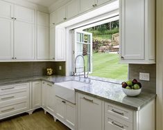 a bowl of fruit is sitting on the counter top in this kitchen with white cabinets