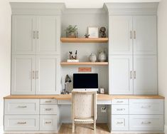 a desk with a computer on top of it in front of some white cupboards