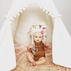 a baby wearing a native american headdress sitting in a teepee