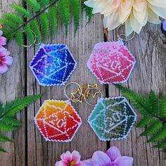 four cross stitch keychains sitting on top of a wooden table next to flowers