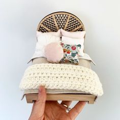 a hand is holding up a small bed made out of an old book and some pillows