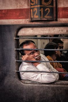 a man sitting in the window of a train looking out at another person on his cell phone