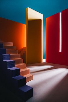 an empty room with blue, red and yellow stairs leading up to the second floor