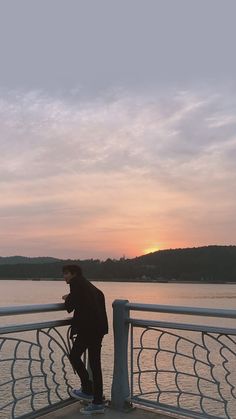 a man standing on the side of a boat looking at his cell phone as the sun sets