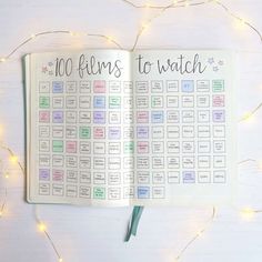 an open planner with the words 100 films to watch written on it and lights in the background