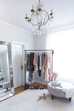 a white room with a chandelier, mirror and clothes on hangers in it