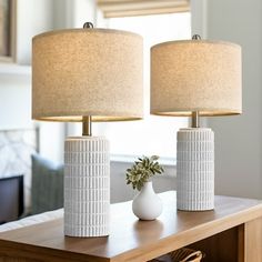 two white vases sitting on top of a wooden table next to a lamp shade