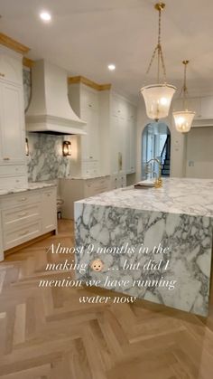 a large kitchen with marble counter tops and white cabinetry, along with a chandelier hanging from the ceiling