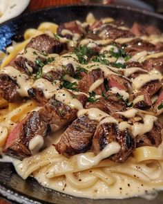 a plate full of pasta with meat and sauce on the top, sitting on a table