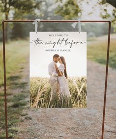 a welcome sign hanging from a metal frame in front of a field with tall grass