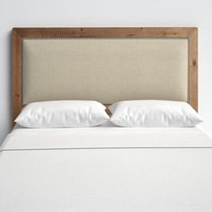 an upholstered bed with white linens and wood headboard, against a white wall