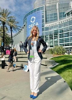 a woman standing in front of a building with her hands on her hips and wearing white pants