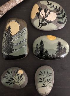 four painted rocks sitting on top of a wooden table next to a stick and tree branch