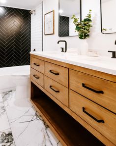 renovated bathroom, black and white bathroom, wooden vanity, black hardware, abstract art, herringbone tile, marble floor, master bathroom,design inspo, flip house inspo, beautiful bathroom Navy White Wood Bathroom, Black Tile Bathroom White Vanity, Oak Vanity Black Hardware, Oak Cabinets With Black Hardware Bathroom, Art For Black And White Bathroom, White And Black Bathroom Floor, Black White And Wood Bathroom Ideas, Black Tile White Tub, Black And Wood Bathroom Vanity