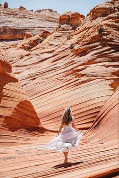 a woman in a white dress is walking through an area with red rocks and cliffs